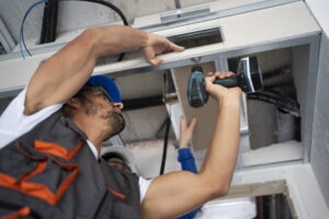 HVAC technician installing ductwork with a power drill during air conditioning repair service