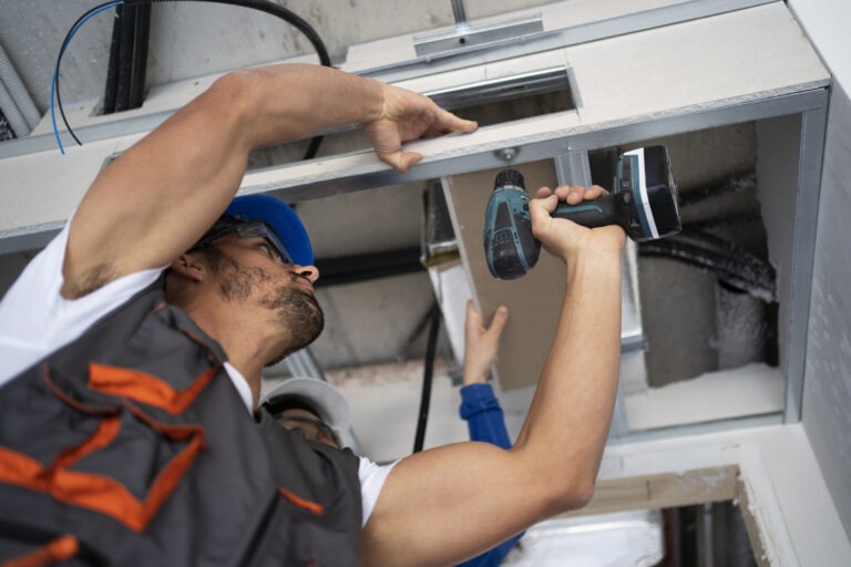 HVAC technician installing ductwork with a power drill during air conditioning repair service